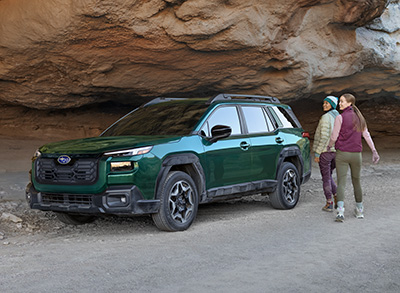 Rear shot of Outback Onyx Edition XT in Autumn Green Metallic parked at overlook and male talent sitting in open trunk holding a tablet.